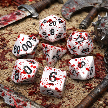 Load image into Gallery viewer, White dice with black numbers, resembling blood, on a surface with weapons and red stains.